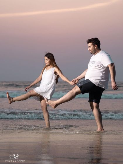 A fun and playful moment on a Goa beach, capturing the couple kicking up water at sunset during their pre-wedding shoot.