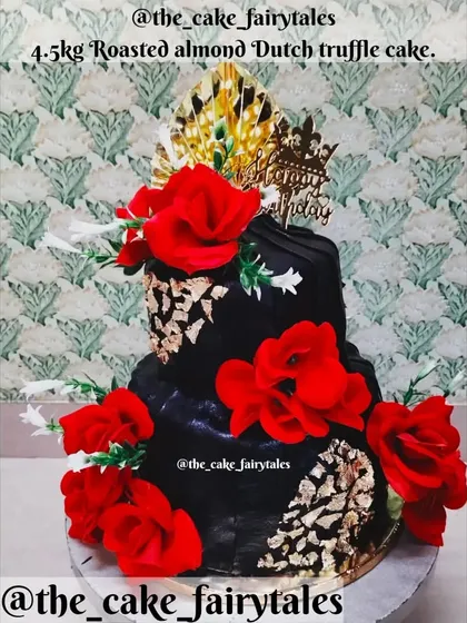 For a grand celebration, this 4.5kg two-tiered Roasted Almond Dutch Truffle cake makes a statement. It features a bold black finish with gold leaf accents and is decorated with vibrant red flowers.