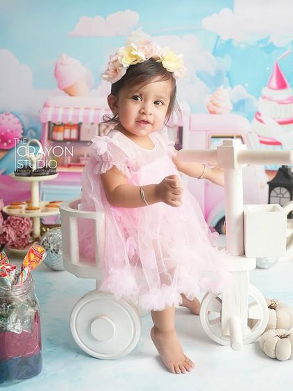 Sitting pretty on a little white tricycle, this one-year-old is ready to ride through her Candyland dream.