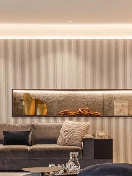 This living room corner exudes warmth and sophistication. We used a fluted wall panel to add subtle texture, enhanced by soft, indirect cove lighting. A recessed wall niche with its own backlighting creates a perfect display for decorative objects, showing how lighting can be used to craft mood and highlight details.