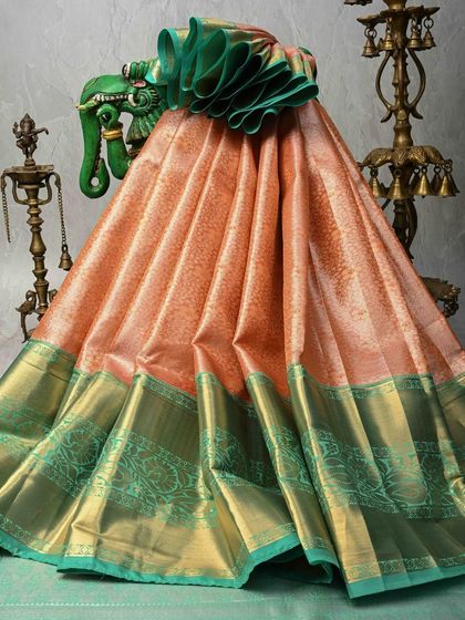 A beautiful peach Kanjivaram silk saree with a contrasting sea-green border. The body has a subtle texture from the weave, and the wide gold and green border adds a touch of opulence.