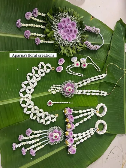 This flat lay shows a complete floral jewellery set in purple and white, crafted for a baby shower. It includes a choker, long necklace, bajuband, and hair accessories.