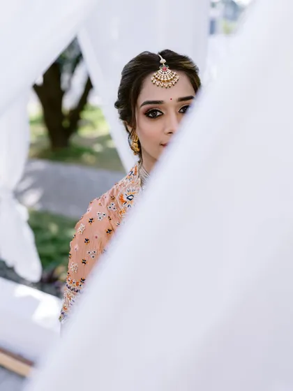 An artistic shot through white drapes, creating a dreamy and ethereal portrait of the bride on her special day.
