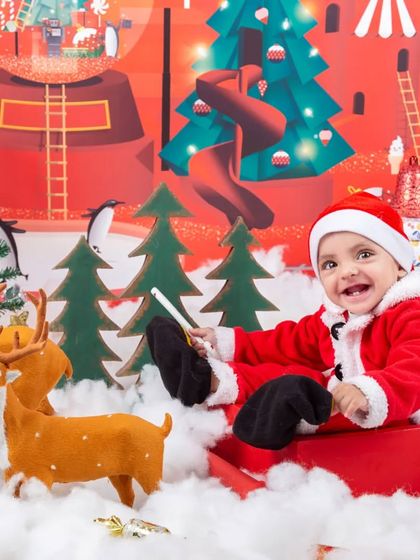 A happy baby Santa enjoying a ride in his sleigh through a Christmas village.