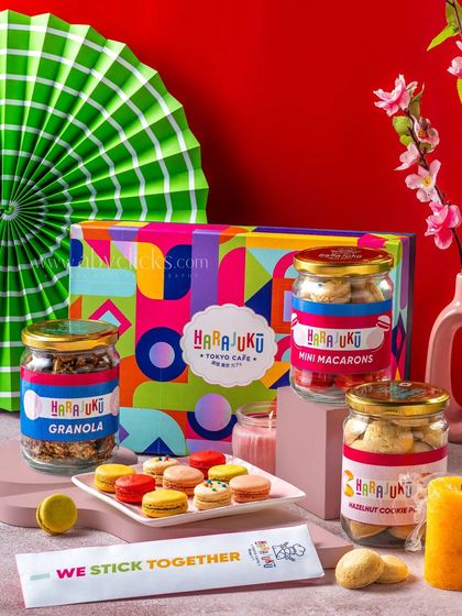 A Harajuku Tokyo Cafe gift box, styled with fresh flowers and a green paper fan against a bold red background.