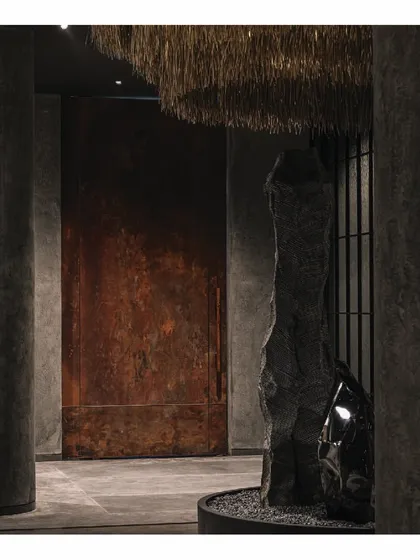 Another view of the grand copper door and the rock installation at the 'Frozen' entrance. The contrast between the warm, rusted metal and the cool, dark stone creates a powerful material dialogue that is central to the store's Zen-inspired theme.