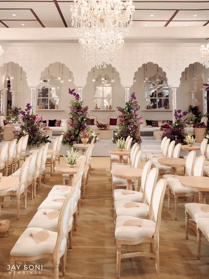 The main seating area for the ceremony, with rows of classic white chairs leading towards a beautifully decorated lounge space under magnificent chandeliers.