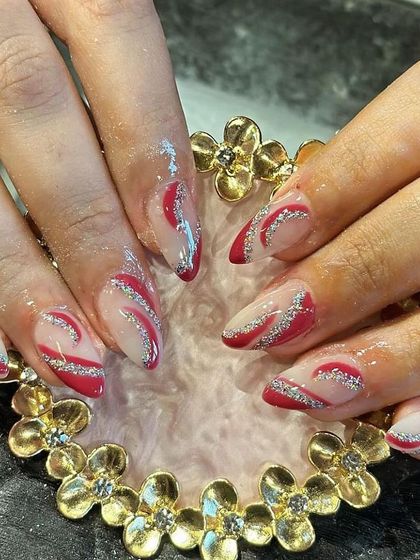 A dynamic design with red and silver glitter waves over a neutral base on almond-shaped nails.