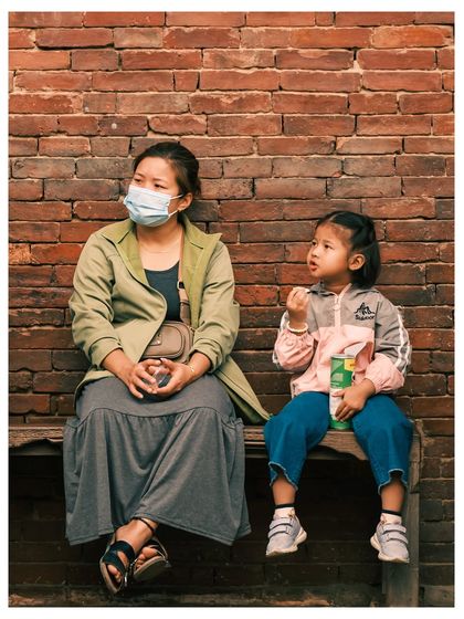 A mother and child sit on a bench against a brick wall in Kathmandu, a candid moment of everyday life.