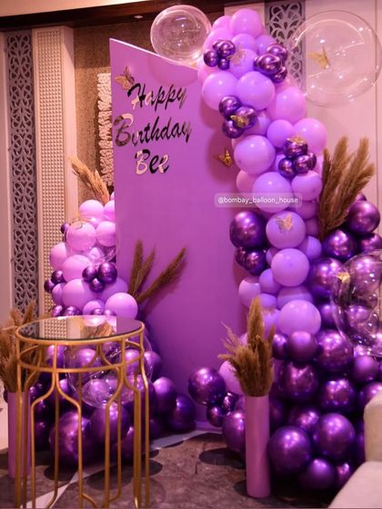 A modern and minimalist purple-themed backdrop, accented with pampas grass and a mix of matte and chrome purple balloons.