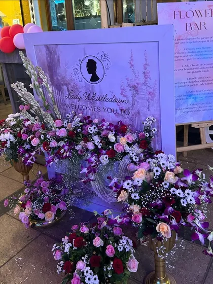 A grand floral entrance for the Bridgerton-themed event, with a 'Lady Whistledown' welcome sign and opulent arrangements in gold urns.