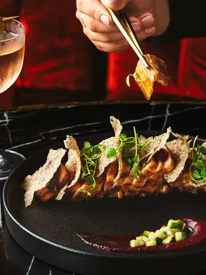 An interactive shot from the Akina Mumbai series, with chopsticks picking up a piece of sliced pork belly. This adds a human element and sense of action, complemented by a beautifully crafted cocktail.