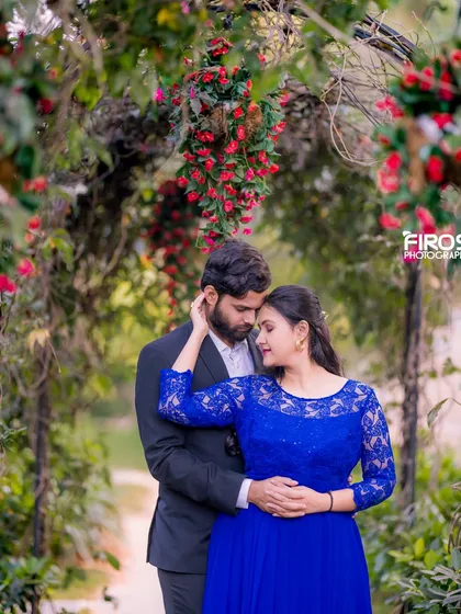 An intimate couple's portrait under a beautiful archway covered in red flowers and green vines, creating a romantic and secluded garden feel.