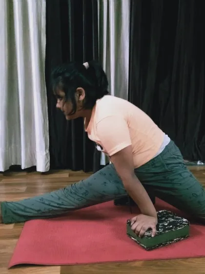 A young practitioner uses a block to assist her in a front split stretch. This helps maintain proper hip alignment while gradually opening the hamstrings.