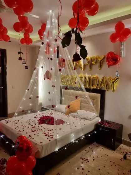 The bed adorned with a fairy light canopy, scattered rose petals, and hanging roses.