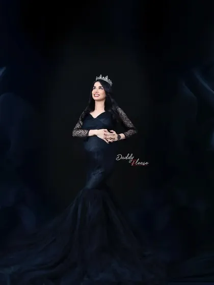 A regal and dramatic portrait of a mother-to-be in a black mermaid gown, complete with a crown. The dark, flowing fabric surrounding her creates a majestic and powerful image.