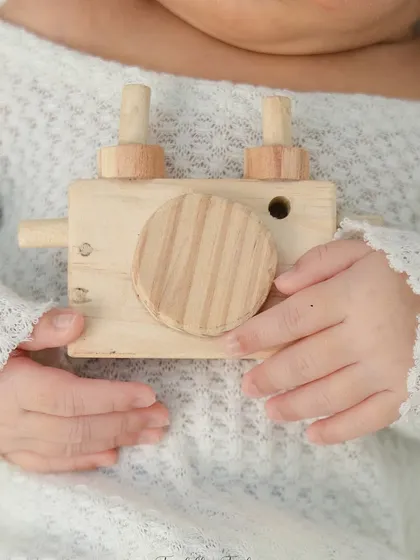 A newborn's tiny hands holding a miniature wooden camera. This playful detail adds a creative touch, symbolizing the beginning of a life of captured memories.