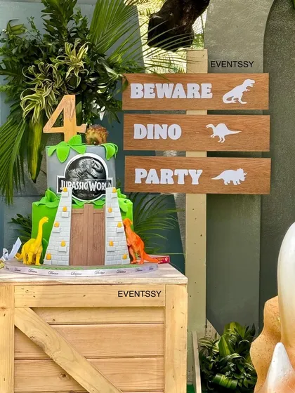The Jurassic World themed cake, complete with the iconic gate design, sits on a rustic wooden crate.