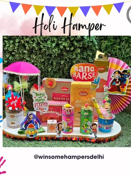 A delightful Holi hamper set against a green backdrop. This tray is filled with "Rang Barse" themed goodies, including snacks, thandai, and buttermilk, and decorated with a miniature umbrella and festive cutouts.