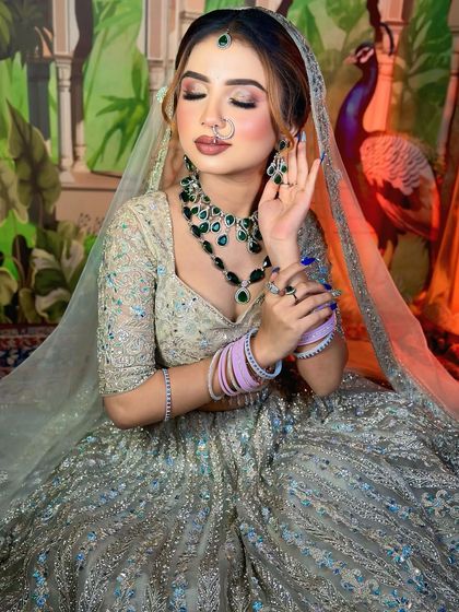 A modern bridal look with a silver-grey lehenga and emerald jewelry. The makeup can be customized with a nude or a bold red lip.