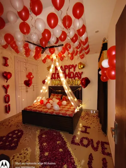 I create romantic birthday surprises at home, like this complete room decoration. It features a canopy with fairy lights over the bed, red and white balloons on the ceiling, and rose petals on the floor spelling out "I LOVE YOU".