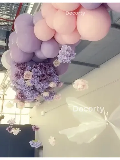 An artistic shot of the ceiling decor, featuring a cascade of pink and purple balloons mixed with floral arrangements and hanging butterflies.