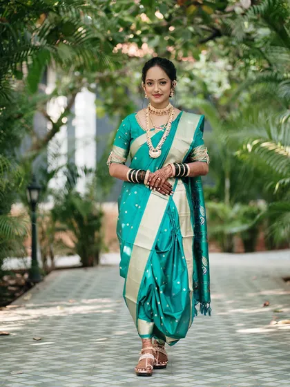 A full-length portrait of a bride in a stunning teal Nauvari saree. Her confident pose and direct gaze make this a powerful and elegant image, showcasing traditional bridal fashion.