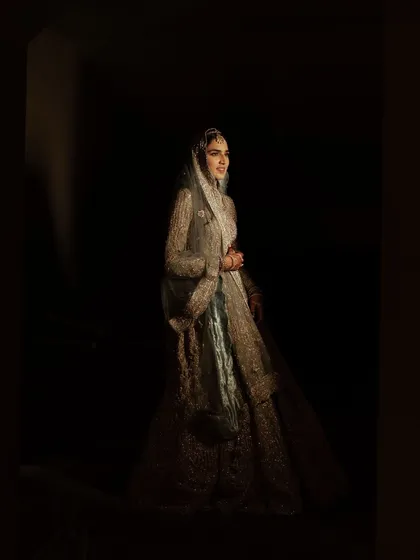 A full-length portrait using dramatic, low-key lighting. The bride emerges from the shadows, creating a powerful and theatrical image that feels timeless.