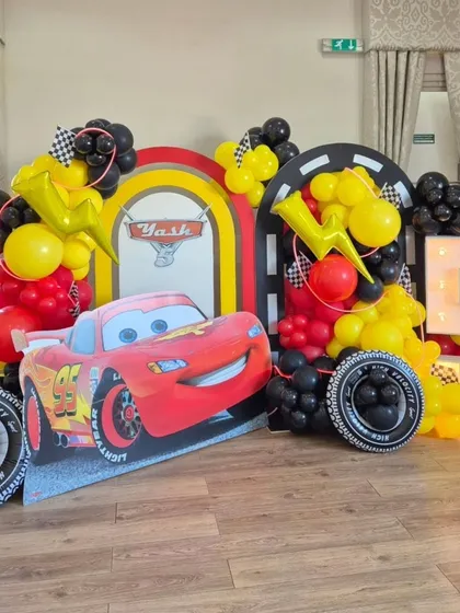 The main photo backdrop for the Cars party, featuring a large character cutout, tire props, and a marquee number.