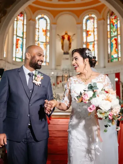The newlyweds walking down the aisle of a beautiful church with stunning stained-glass windows. A classic and joyful "just married" moment.