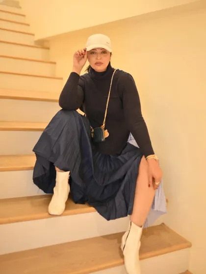 A cozy winter look with a turtleneck, pleated skirt, and white boots. The baseball cap adds a casual, sporty edge.