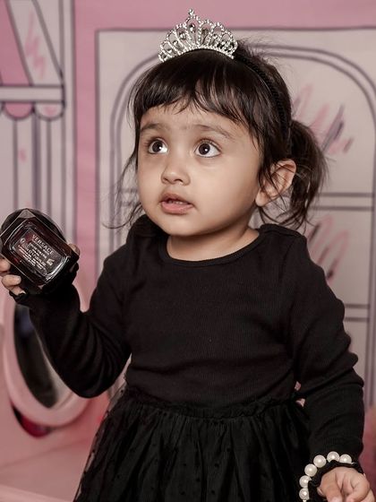 A fun and fashionable shoot with a pink Parisian-themed backdrop. This little girl is playing dress-up with a tiara, looking like a little princess.