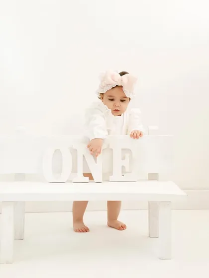 Another angle from the all-white first birthday set, showing the little girl's curiosity as she reaches for the letters.