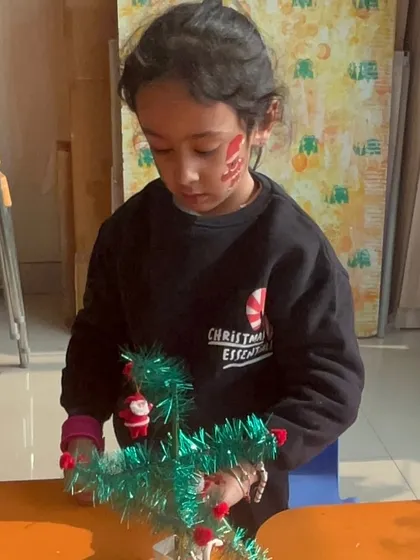 A student carefully decorates a miniature Christmas tree, a perfect craft for little hands.