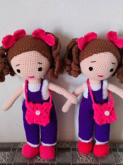 Two twin dolls in matching purple jumpsuits and pink bags. Perfect for sisters or best friends.