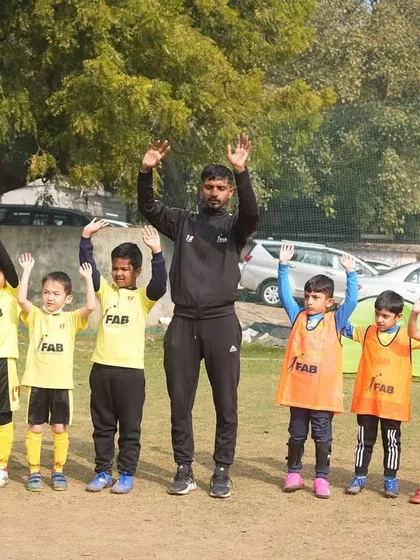 A coach and players with their hands up. We are dedicated to nurturing a love for football and fostering growth both on and off the field.