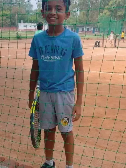 A young player smiling by the court. We aim to create a positive and encouraging atmosphere where kids feel happy and motivated to play.
