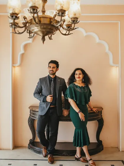 A stylish portrait of the couple posing by a vintage console table under an ornate chandelier. Their formal attire and the elegant setting create a look of classic sophistication.