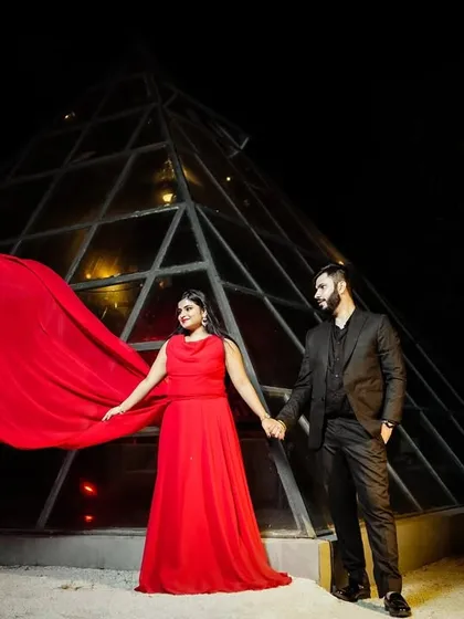 A powerful pre-wedding stance. The couple holds hands in front of a lit pyramid, with the bride's red dress creating a striking visual against the night sky.