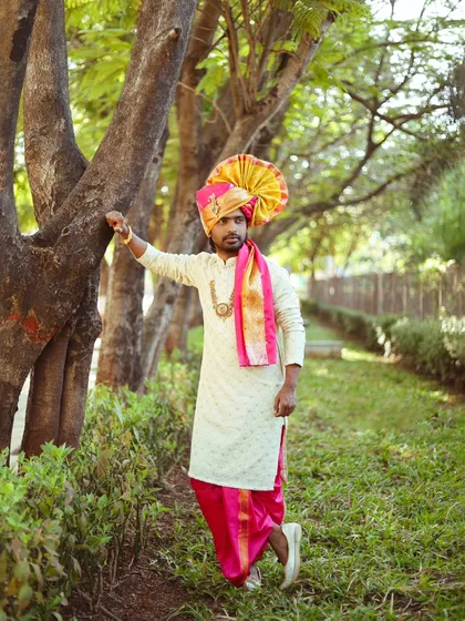 An outdoor portrait of a groom in traditional Maharashtrian attire, complete with a vibrant pheta (turban). The natural setting adds a lovely, soft feel.