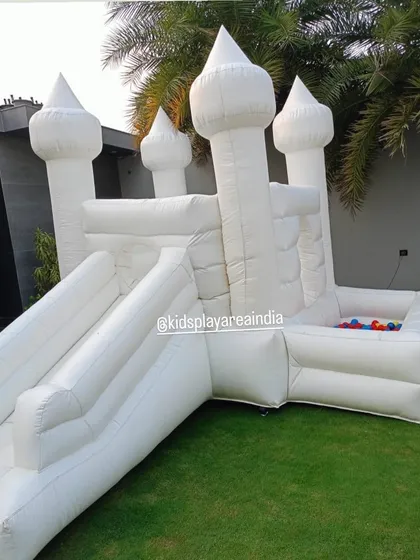 A side view of our 4-in-1 white castle, showing the slide and the attached ball pit area, set up on a lush green lawn.
