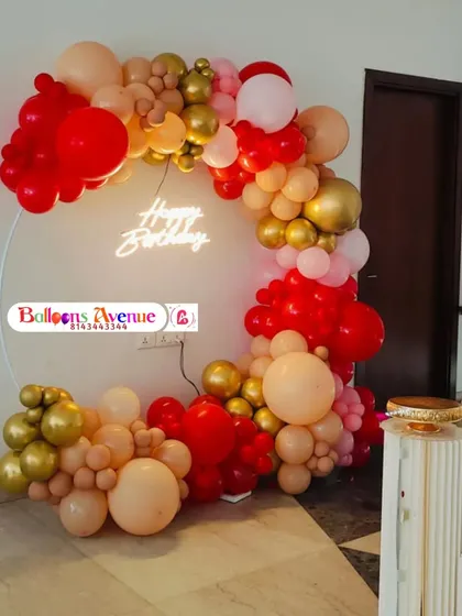 A bold and vibrant birthday decoration with a balloon arch in red, gold, and peach tones on a circular frame.