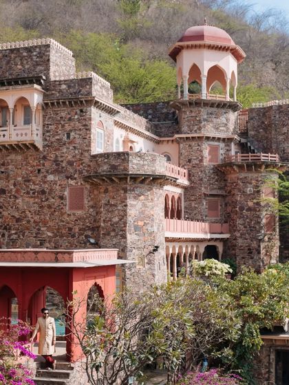 The groom stands against the rustic, historic stone architecture of Neemrana Fort-Palace, a venue that offers a majestic backdrop for wedding portraits.