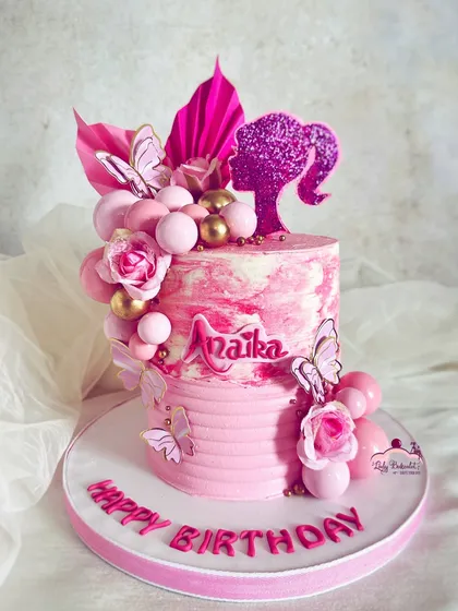 A modern and chic take on the Barbie theme. This cake uses a marbled pink buttercream effect, a glittery silhouette topper, and a cascade of pink and gold spheres and butterflies.