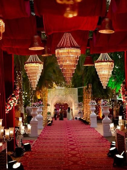 A royal entrance fit for a king and queen. This grand walkway features rich red drapes, magnificent tiered chandeliers, and candlelit pathways, setting a majestic tone for the wedding night.