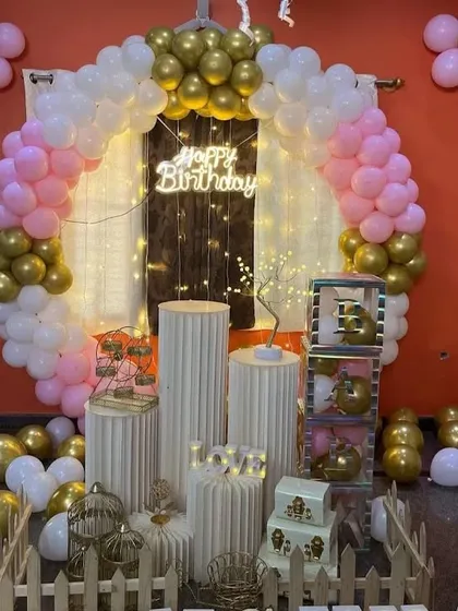 A pink, white, and gold balloon arch with numerous props like a Ferris wheel, birdcages, and gift boxes.