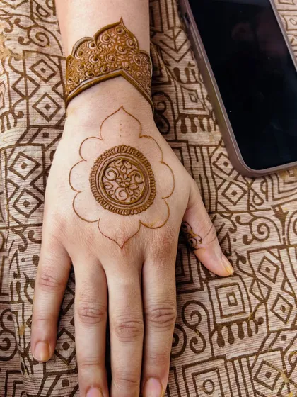 A work-in-progress shot of the mandala design, showing the fresh henna paste and the reference photo on the phone.