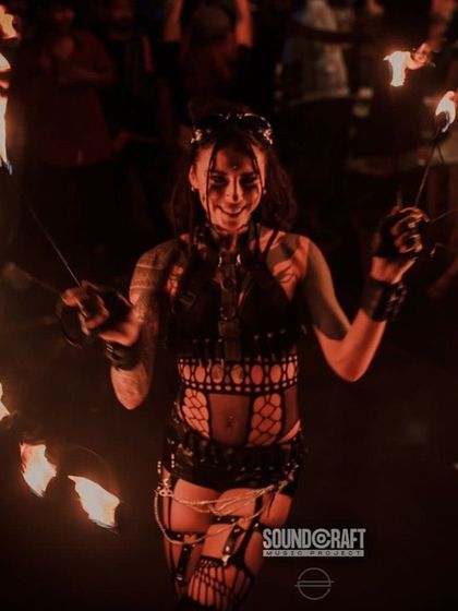 A female fire dancer smiles as she spins two sets of fire poi, surrounded by the glow. We believe in connecting with the audience, sharing the joy and energy of the performance.