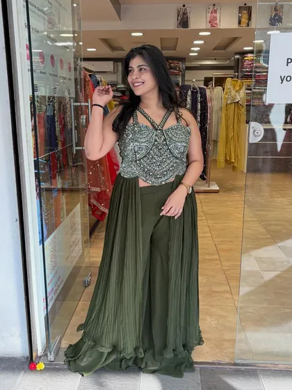 This olive green Indo-Western outfit features a heavily embellished crop top with attached drapes and flowy pants. It's a modern and chic look for a cocktail party.