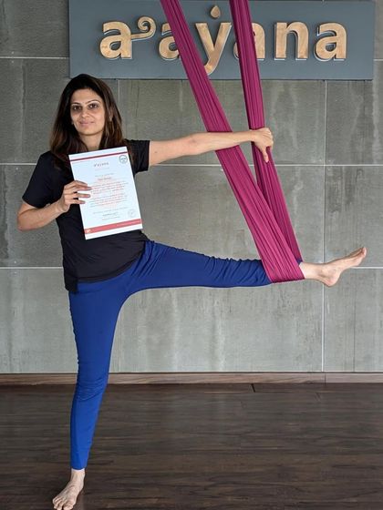 A graduate holds her certificate while demonstrating a pose, ready to start her teaching journey.
